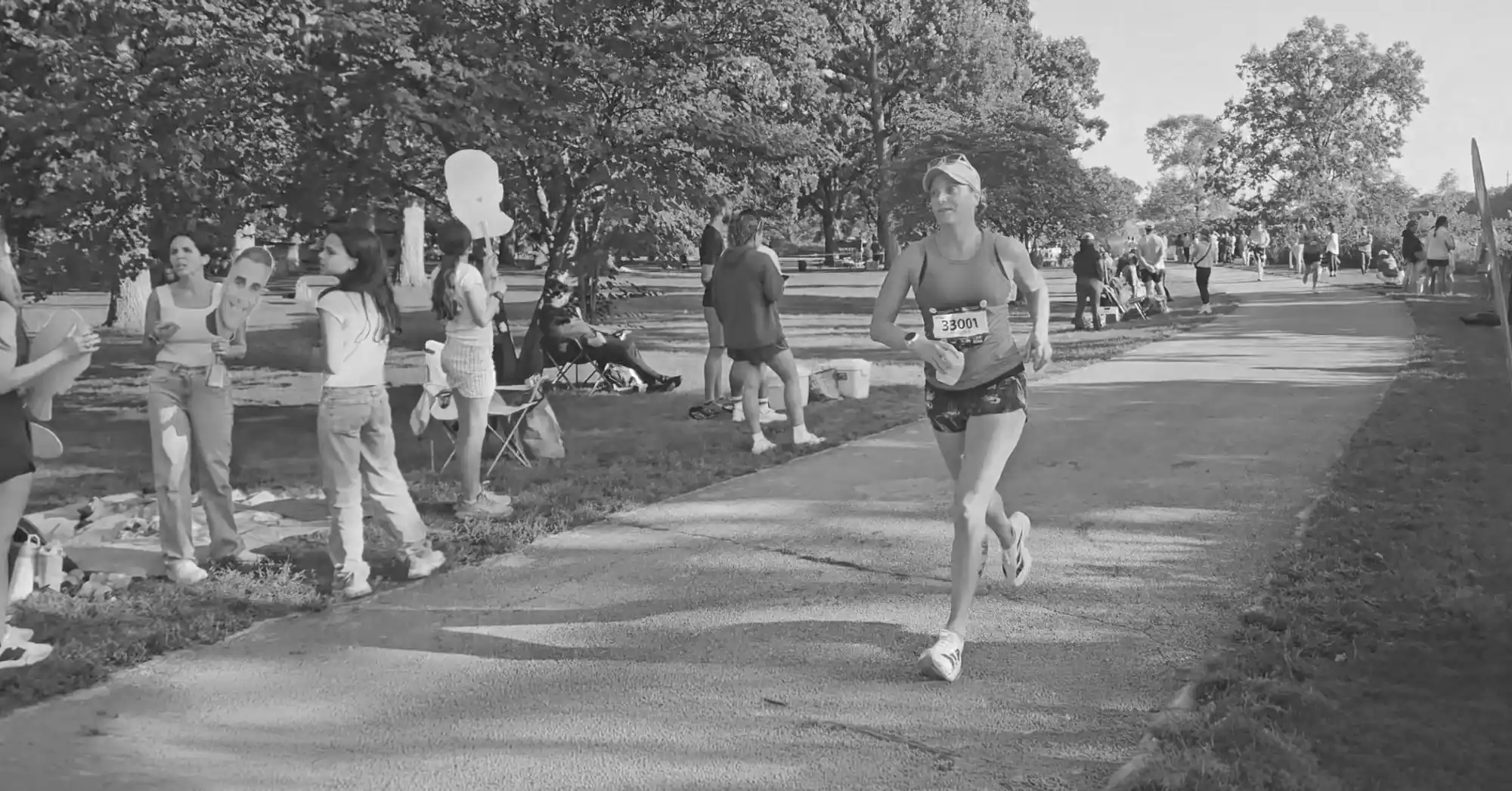 Black-and-white photo of Nicole running along a tree-lined park path during a race as spectators cheer